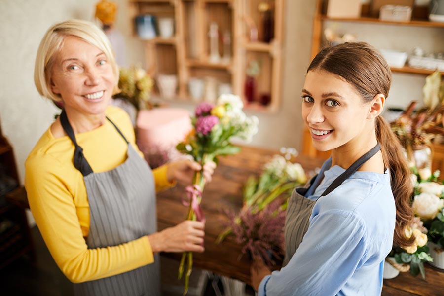 Business Insurance - Two Women Running a Flower Shop Hold Showers and Wear Aprons Behind Their Counter